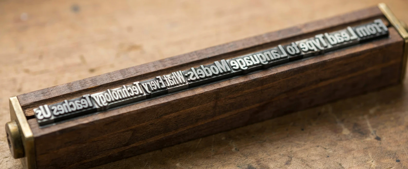 Mirror-image metal type in a wooden holder with brass ends on a worn, ink-stained workbench, spelling out the article title “From Lead Type to Language Models”
